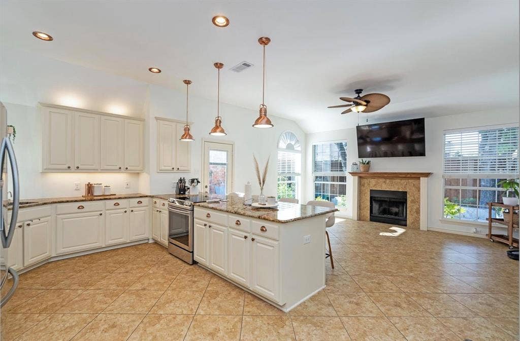 1944 Vantage Drive, Plano, TX 75075 Open-concept living space with a kitchen island, recessed lighting, tile flooring, and a fireplace with a stone surround