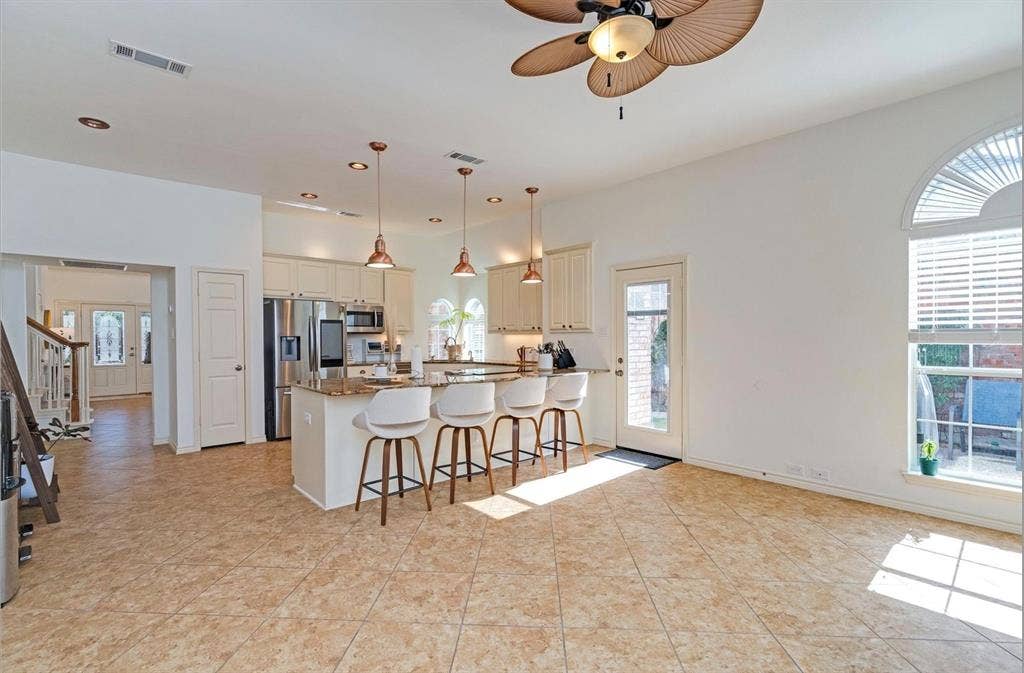 1944 Vantage Drive, Plano, TX 75075 Tile flooring extending throughout, kitchen island with seating, stainless steel appliances, upper and lower cabinetry, and an arched window