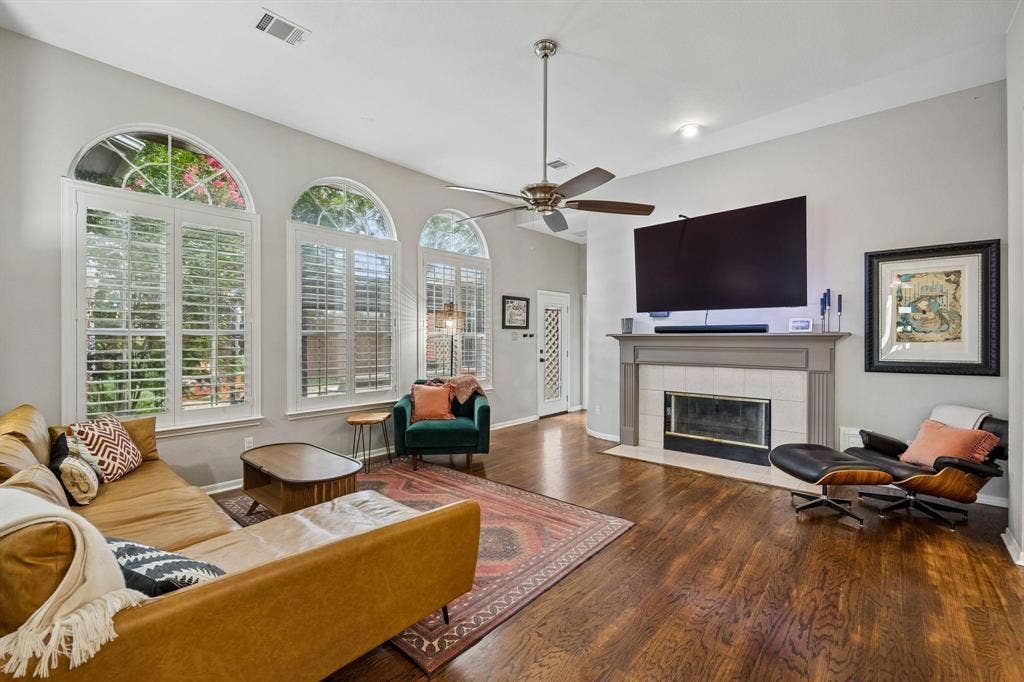 3104 Congress Avenue, Plano, TX 75025 Arched windows with plantation shutters, wood-finish flooring, vaulted ceilings, a ceiling fan, and a fireplace with a tile surround and mantel