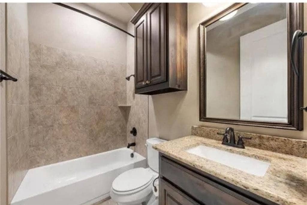 2313 Therese, Waco, TX 76712 Bathroom featuring a built-in tub with tile surround, a built-in vanity with a granite-style countertop, a rectangular undermount sink, and a framed wall mirror