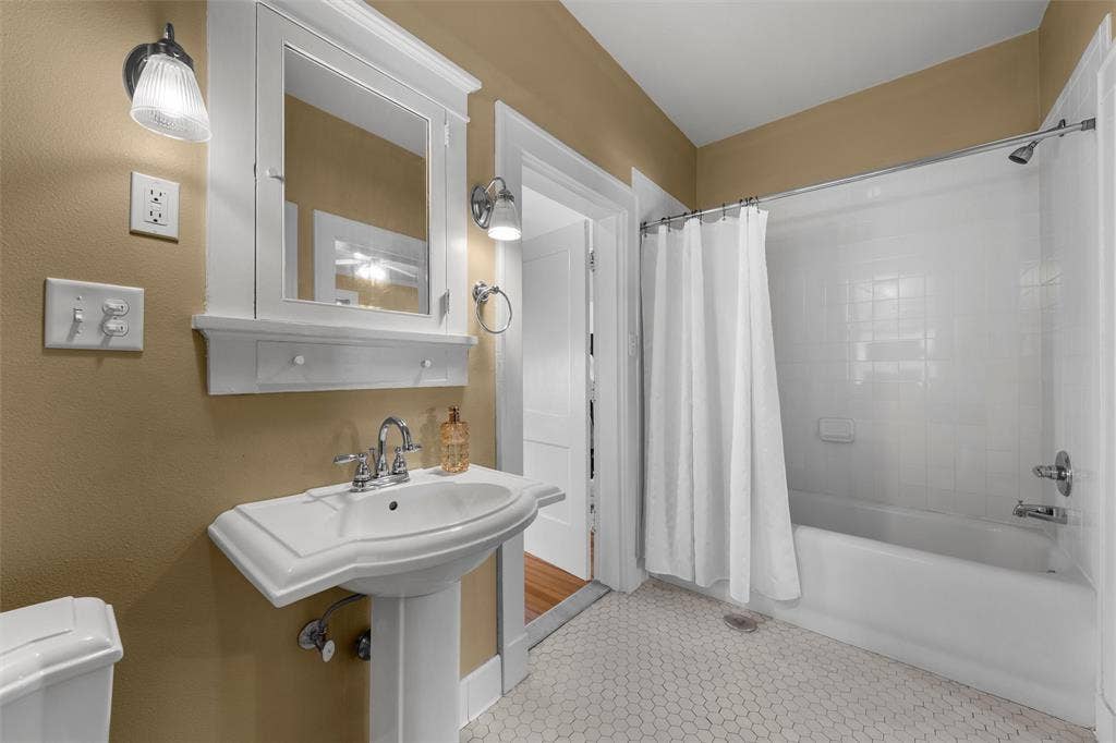 2424 Austin Avenue, Waco, TX 76701 Pedestal sink with chrome faucet, framed medicine cabinet, wall-mounted light fixtures, white hexagon tile flooring, and a shower-over-tub combination