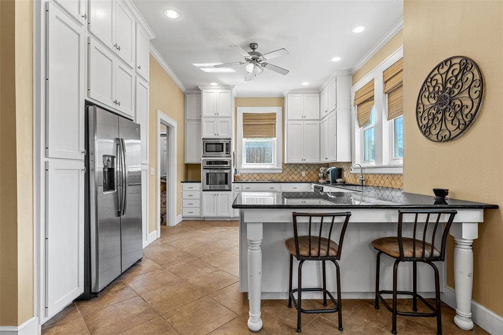 2424 Austin Avenue, Waco, TX 76701 Spacious kitchen featuring white cabinetry, integrated stainless steel appliances, a large island with counter seating, neutral-toned tile flooring, and a decorative tile backsplash