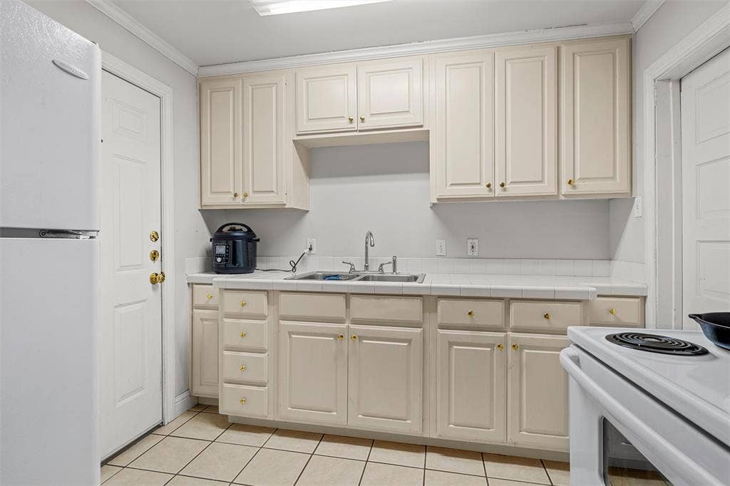 2424 Austin Avenue, Waco, TX 76701 Kitchen featuring white cabinetry with gold-toned hardware, a stainless steel double basin sink, and a white tile backsplash