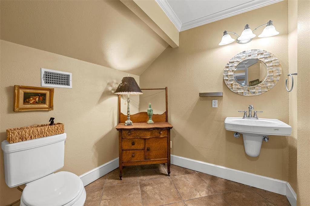 2424 Austin Avenue, Waco, TX 76701 Wall-mounted sink with brushed nickel faucet, oval mirror with textured frame, three-light vanity fixture, crown molding, and tiled flooring