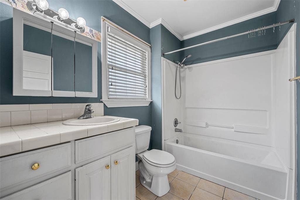 2424 Austin Avenue, Waco, TX 76701 Vanity with white cabinetry and tiled countertop, recessed sink with chrome faucet, and a wall-mounted mirrored medicine cabinet
