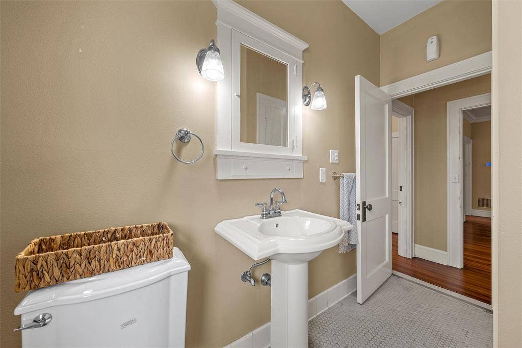 2424 Austin Avenue, Waco, TX 76701 Pedestal sink with chrome faucet, wall-mounted mirror with integrated shelving, and dual sconce lighting