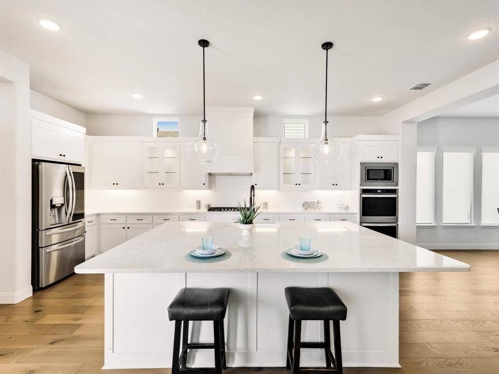 508 N Pecan Parkway, Northlake, TX 76247 Gourmet kitchen with stainless steel appliances, white cabinetry, a large center island with a light-colored countertop, and wood-finish flooring