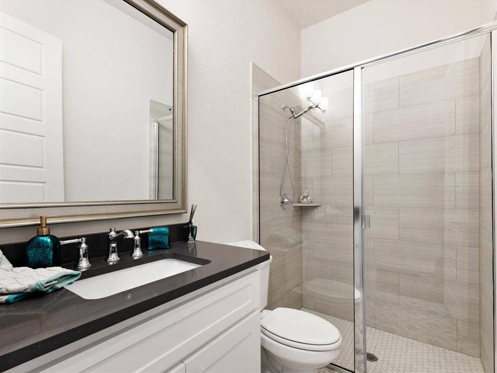 508 N Pecan Parkway, Northlake, TX 76247 Vanity with dark countertop and undermount sink, framed mirror, and glass-enclosed shower with tiled walls and hexagonal floor