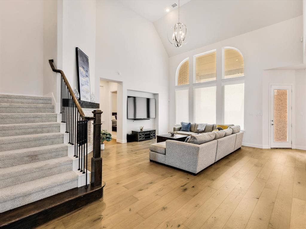 508 N Pecan Parkway, Northlake, TX 76247 Soaring vaulted ceiling with a contemporary chandelier, large arched windows, light wood-finish flooring, and a carpeted staircase with dark wood and iron railing