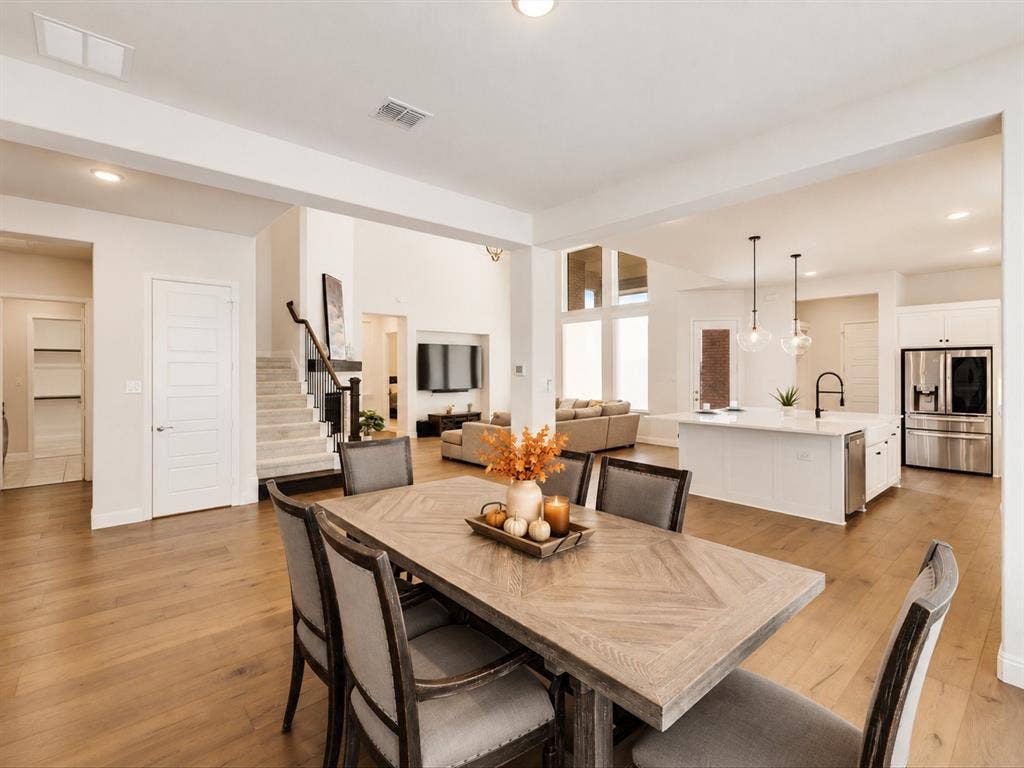 508 N Pecan Parkway, Northlake, TX 76247 Open-concept design featuring wood-finish flooring, white kitchen cabinetry, a kitchen island with pendant lighting, and a staircase with dark wood handrails