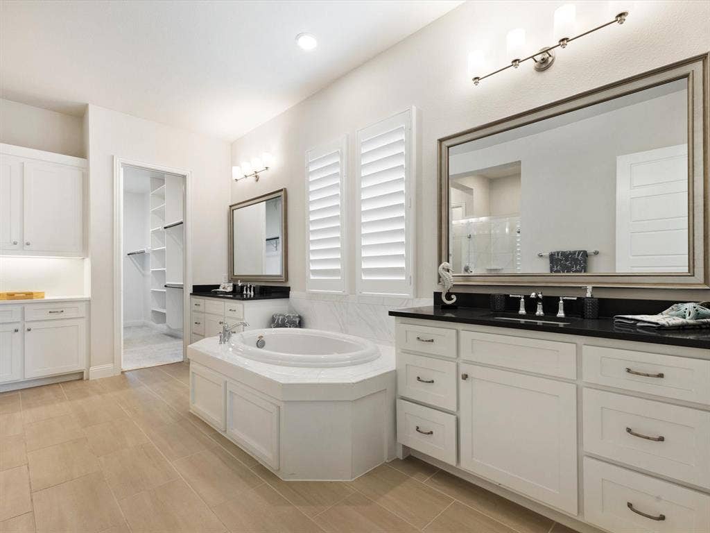 508 N Pecan Parkway, Northlake, TX 76247 Dual vanities with white cabinetry and dark countertops, built-in soaking tub, wood-finish flooring, and a walk-in closet with built-in shelving