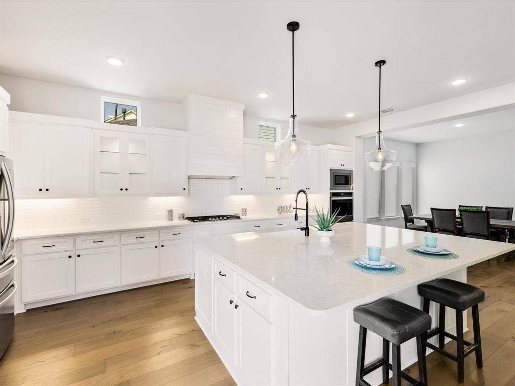 508 N Pecan Parkway, Northlake, TX 76247 Gourmet kitchen featuring a large central island with seating, pendant lighting, white cabinetry, wood-finish flooring, and integrated stainless steel appliances