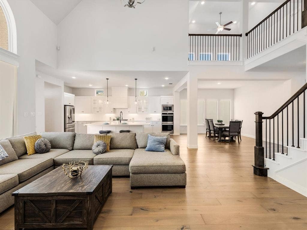 508 N Pecan Parkway, Northlake, TX 76247 Vaulted ceilings, wood-finish flooring, white kitchen cabinetry, open-concept living, and a prominent staircase with dark wood and iron balusters