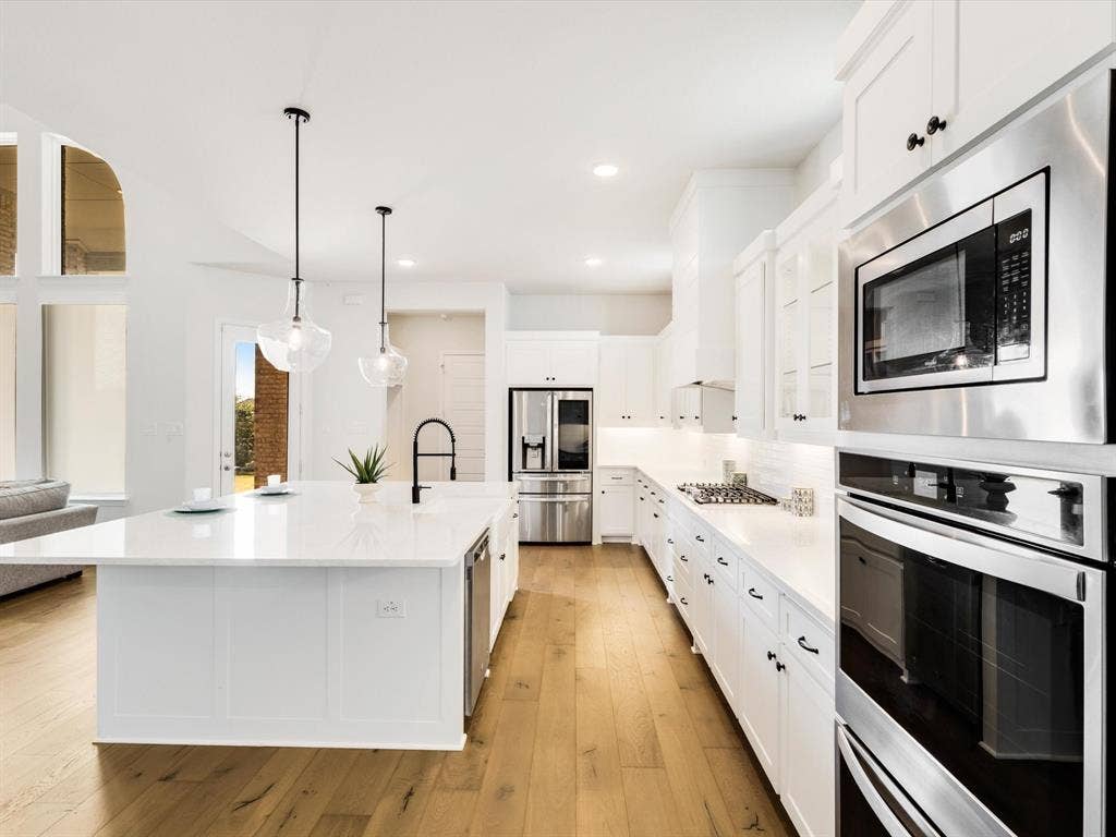 508 N Pecan Parkway, Northlake, TX 76247 Spacious kitchen featuring white cabinetry, stainless steel appliances, a large center island with a sink, and wood-finish flooring