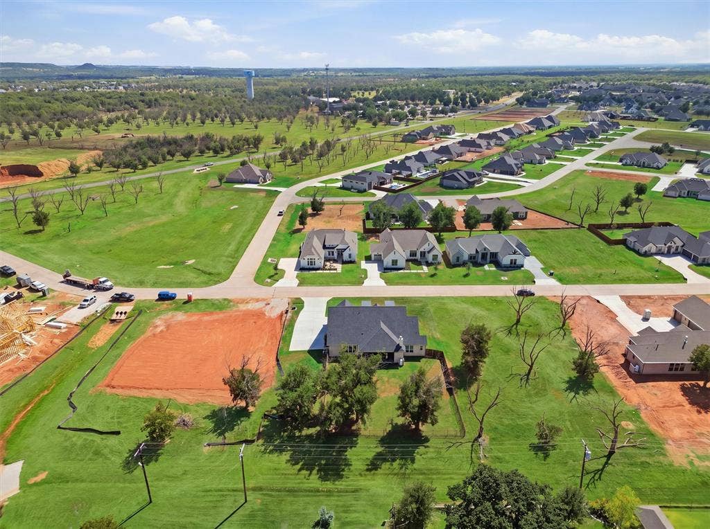 2181 Middlewood Circle, Granbury, TX 76049 Expansive green spaces surround a newly developed residential area featuring various single-story homes and a visible water tower in the distance