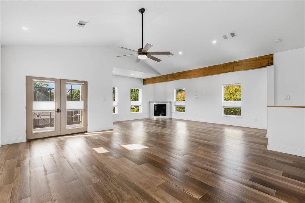 Vaulted ceiling, wood-finish flooring, exposed wood beam, modern fireplace, and double French doors to outdoor space
