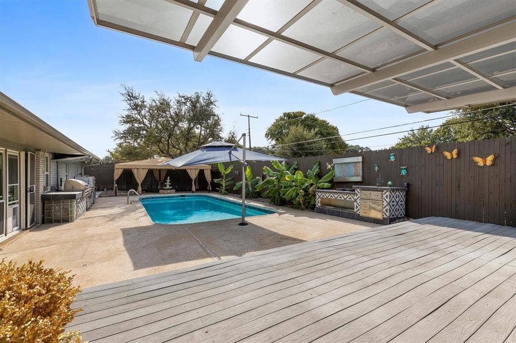 Expansive outdoor area featuring a swimming pool, wood deck, covered patio, built-in outdoor kitchen, and privacy fencing
