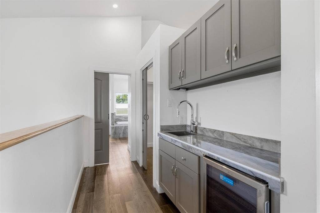 Wood-finish flooring, recessed lighting, built-in cabinetry with a sink, stone countertop, and an integrated beverage refrigerator