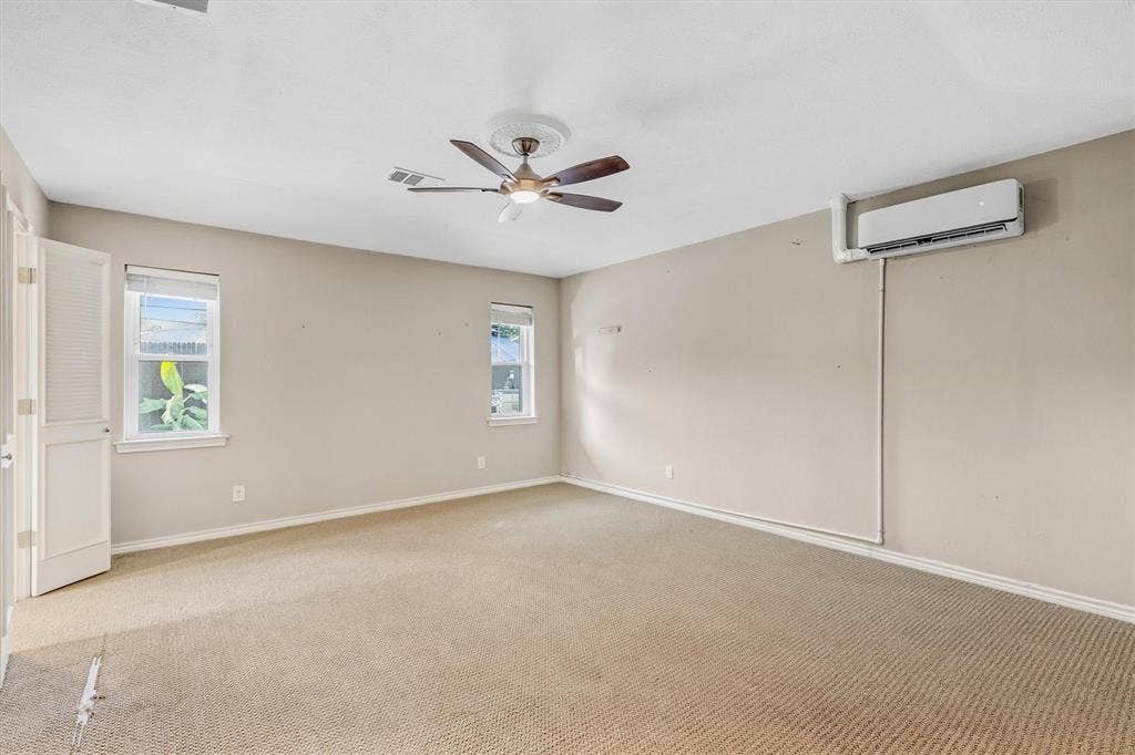 Neutral wall finishes, textured carpeting, two windows, ceiling fan with light fixture, and wall-mounted air conditioning unit