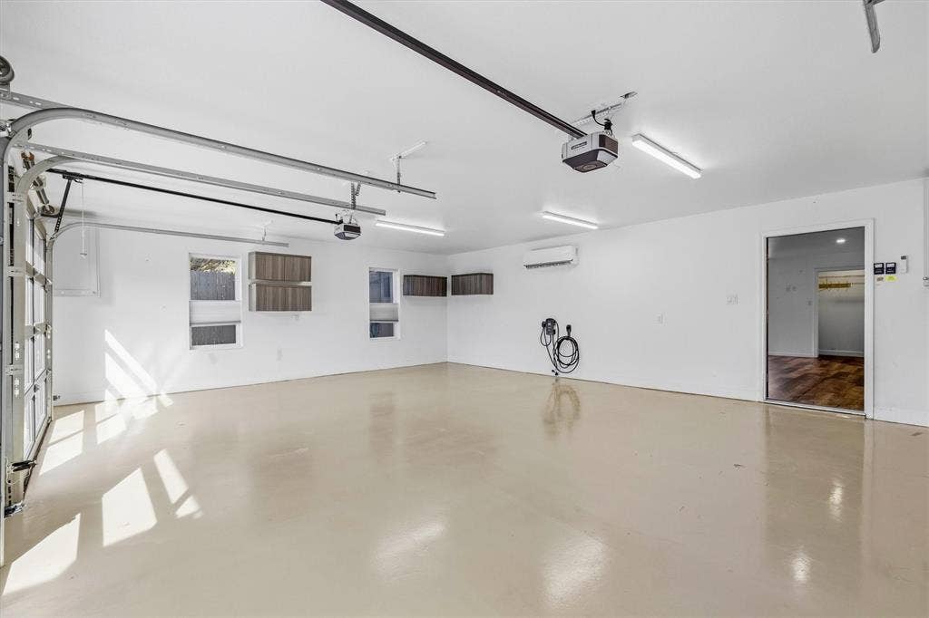 Spacious garage with an overhead door, multiple windows, built-in wall cabinets, and fluorescent ceiling lighting