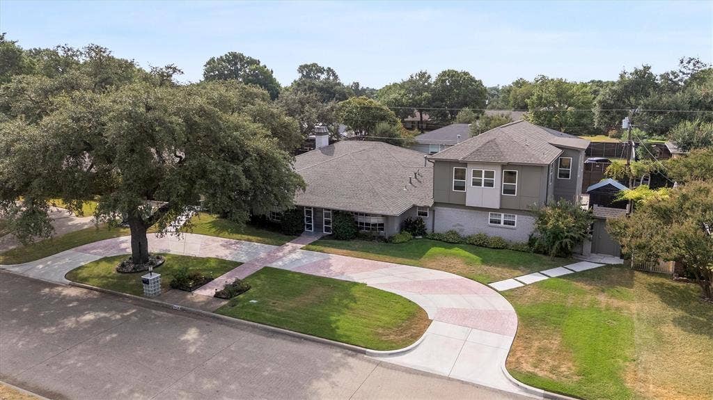 Expansive circular driveway with patterned paving, mature front yard tree, and an additional side entrance