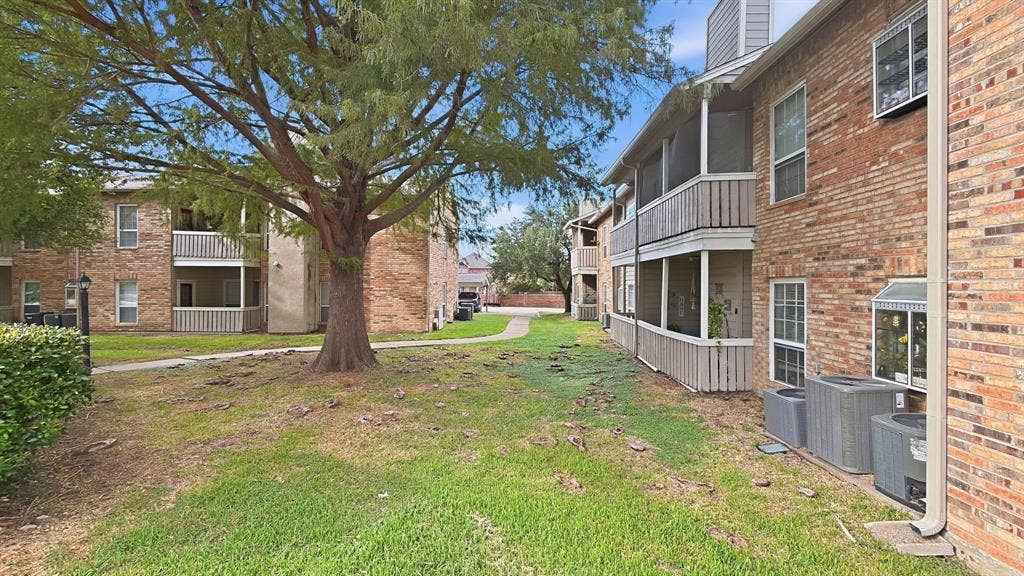 1700 Amelia Court, #126, Plano, TX 75075 Brick exterior with multiple screened balconies, featuring a mature tree and landscaped shrubbery