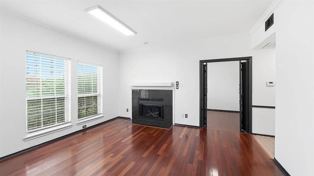 1700 Amelia Court, #126, Plano, TX 75075 Rich wood-finish flooring, a fireplace with a dark-toned surround and white mantel, dual windows with blinds, and a recessed ceiling light fixture
