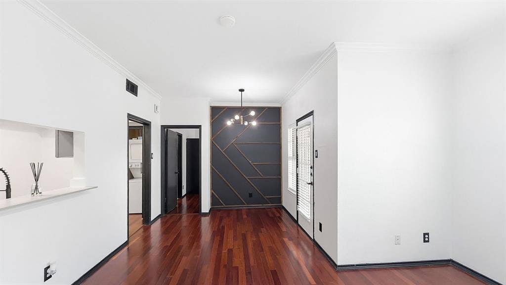 1700 Amelia Court, #126, Plano, TX 75075 Rich wood-finish flooring, accent wall with geometric paneling, modern pendant light fixture, and crown molding