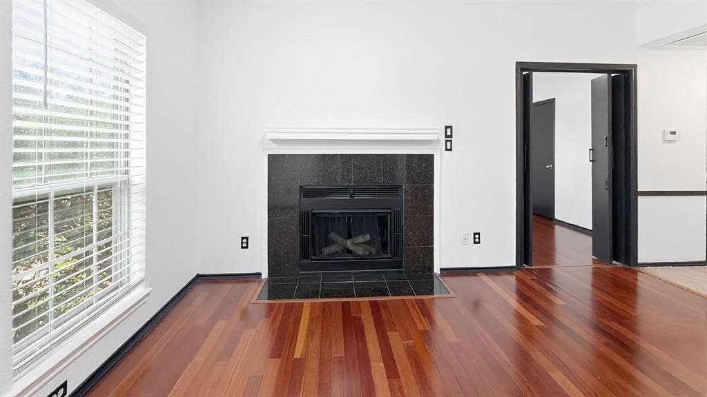 1700 Amelia Court, #126, Plano, TX 75075 Hardwood flooring, black tile fireplace surround, white mantel, and a window with blinds