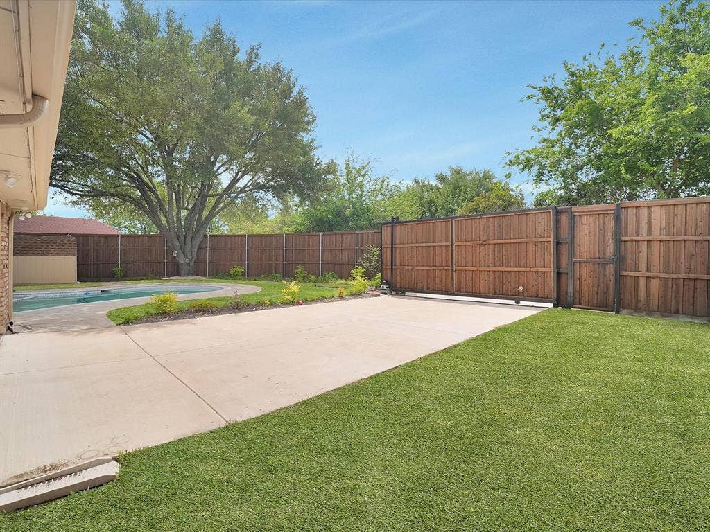 1304 Carriage Creek Drive, DeSoto, TX 75115 Expansive backyard featuring a concrete patio, a swimming pool, a large mature tree, a privacy fence, and a sliding gate