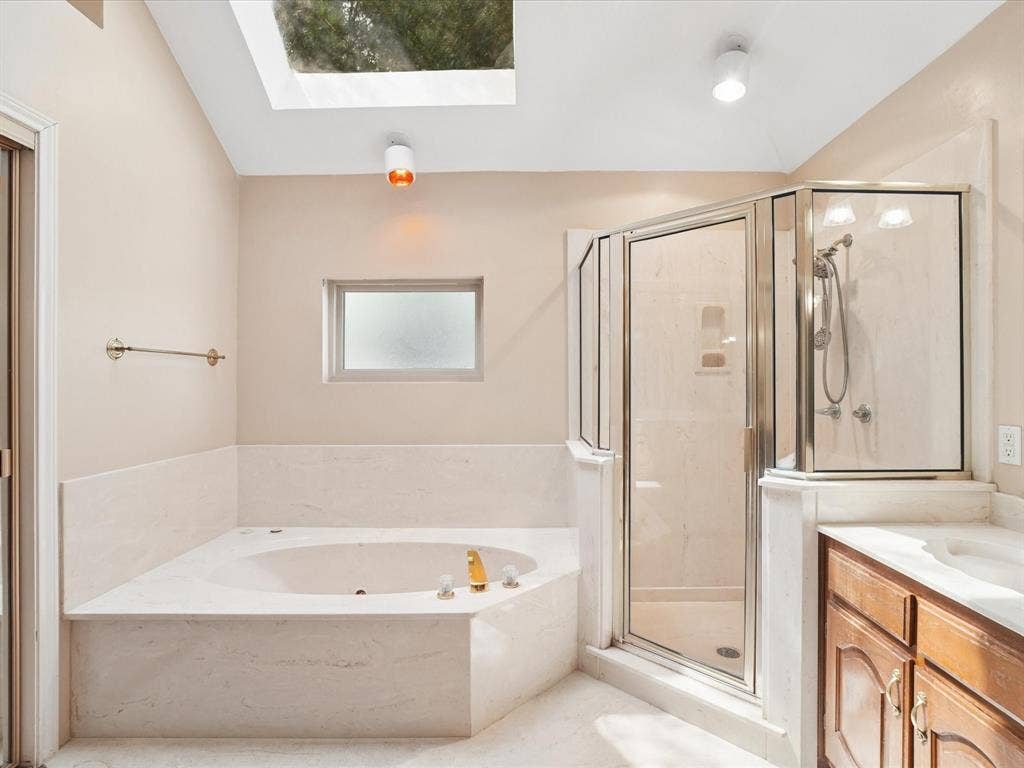 1304 Carriage Creek Drive, DeSoto, TX 75115 Recessed corner tub with integrated jets, glass-enclosed shower, wood vanity with integrated sink, and overhead skylight