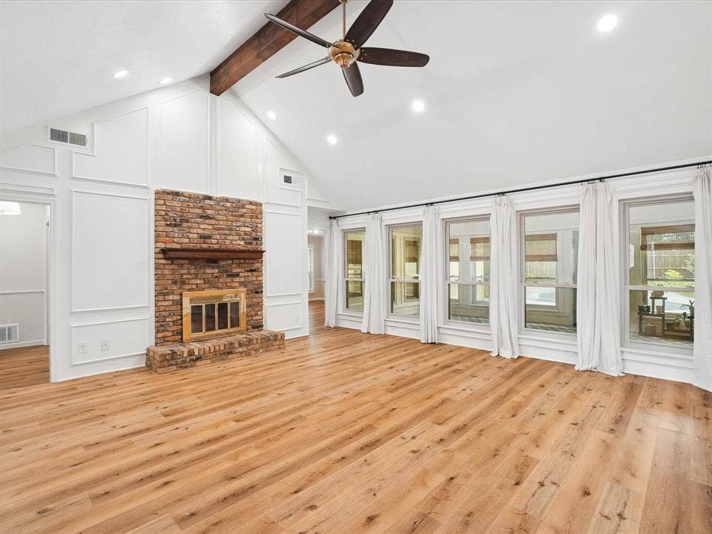 1304 Carriage Creek Drive, DeSoto, TX 75115 Vaulted ceilings with exposed wood beam, recessed lighting, wood-finish flooring, brick fireplace with wood mantel, and a wall of windows