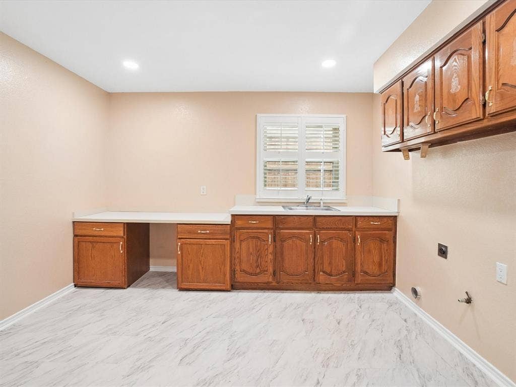 1304 Carriage Creek Drive, DeSoto, TX 75115 Functional utility room featuring wood-finish cabinetry, white countertops, and a stainless steel sink