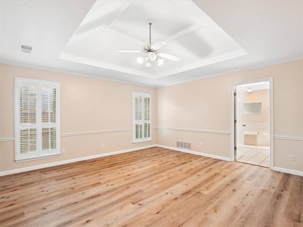 1304 Carriage Creek Drive, DeSoto, TX 75115 Tray ceiling with a ceiling fan, wood-finish flooring, two windows with plantation shutters, and crown molding