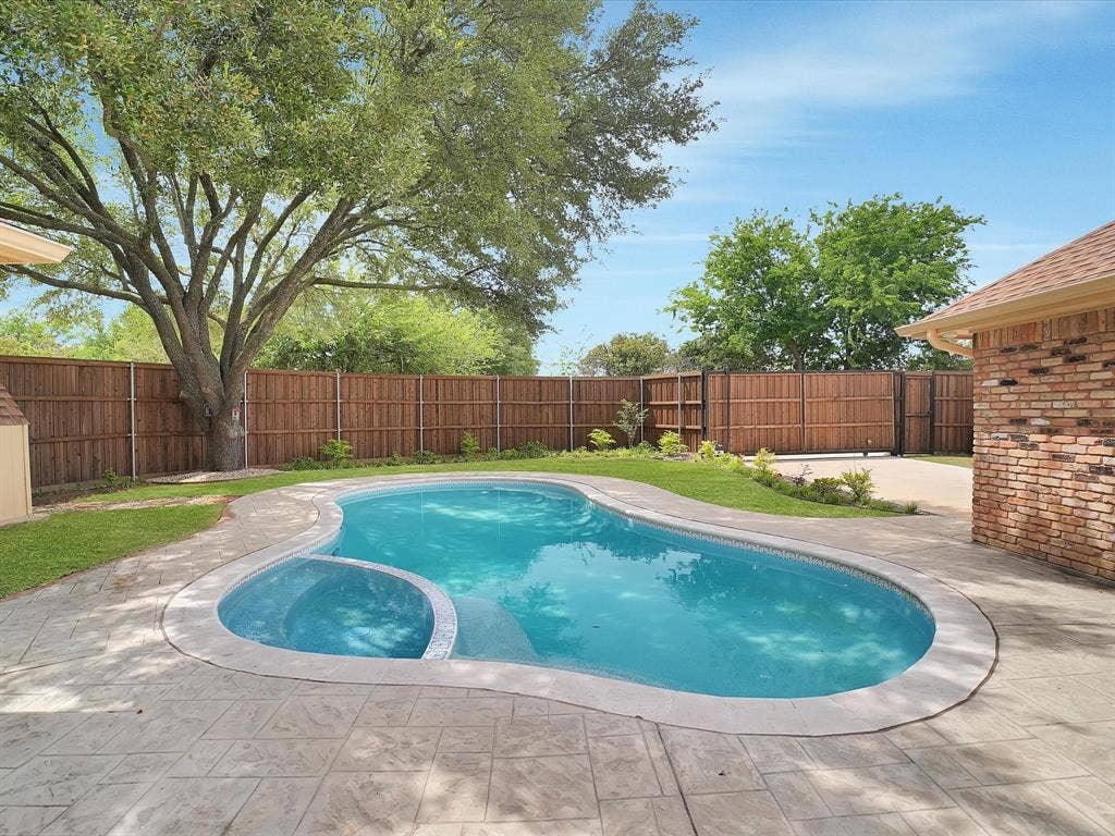 1304 Carriage Creek Drive, DeSoto, TX 75115 Private backyard featuring a free-form swimming pool with integrated spa, stamped concrete decking, mature shade trees, and a wood privacy fence