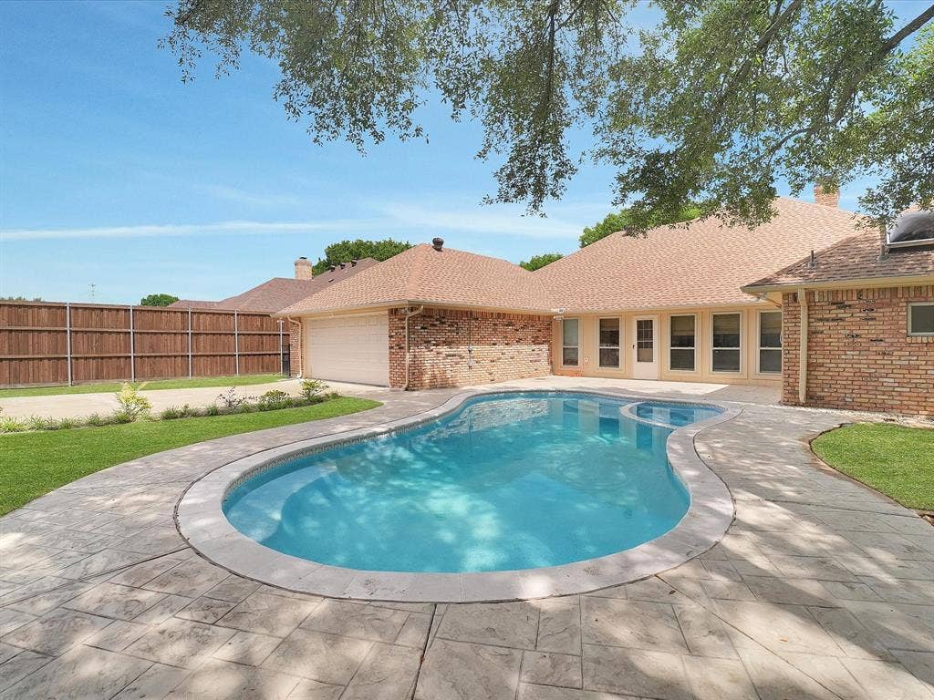 1304 Carriage Creek Drive, DeSoto, TX 75115 Outdoor oasis featuring a freeform swimming pool, stamped concrete decking, and a brick-clad exterior