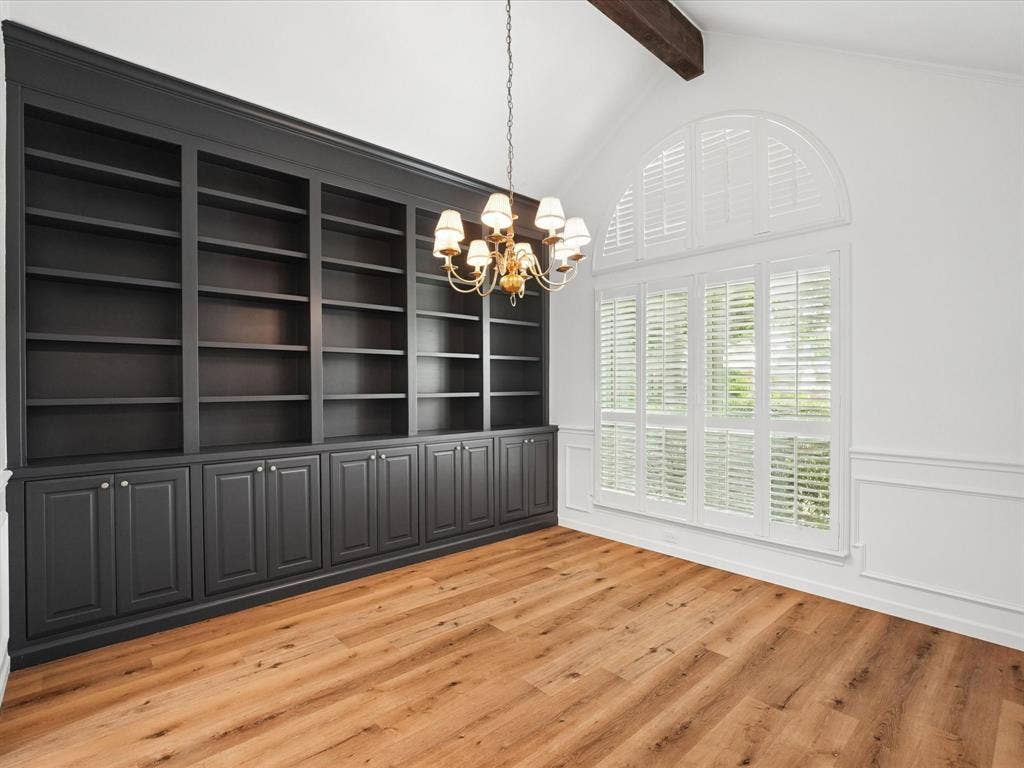 1304 Carriage Creek Drive, DeSoto, TX 75115 Expansive built-in shelving with cabinetry, wood-finish flooring, vaulted ceiling with exposed beam, arched window with plantation shutters, and decorative wall molding