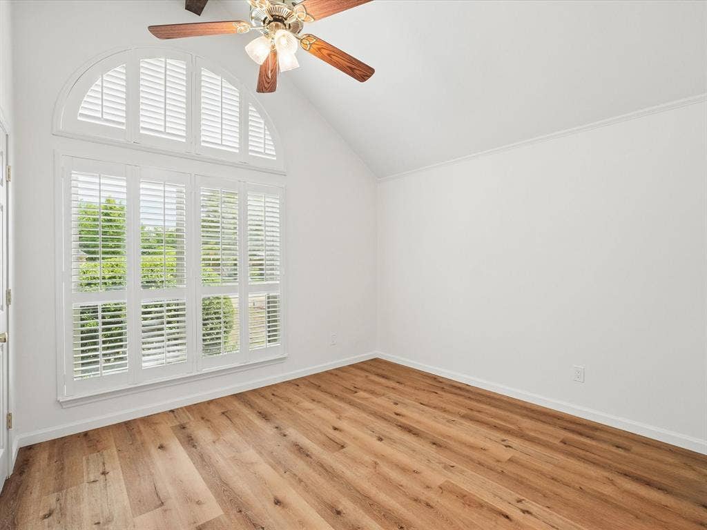 1304 Carriage Creek Drive, DeSoto, TX 75115 Wood-finish flooring, vaulted ceiling, arched window, white plantation shutters, and ceiling fan with lighting fixture
