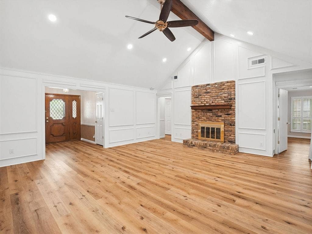 1304 Carriage Creek Drive, DeSoto, TX 75115 Vaulted ceiling with exposed wood beam, recessed lighting, wood-finish flooring, brick fireplace with mantel, and decorative wall paneling