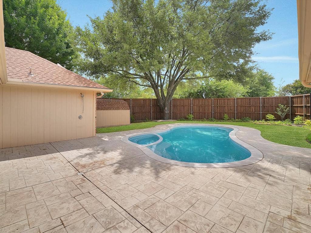 1304 Carriage Creek Drive, DeSoto, TX 75115 Resort-style backyard featuring a free-form swimming pool with integrated spa, stamped concrete patio, and a privacy fence