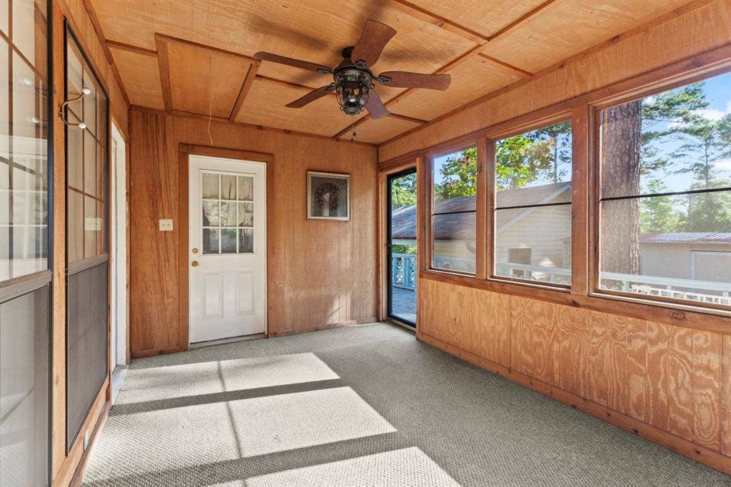 1656 Pineview Lane, Hideaway, TX 75771 Enclosed porch featuring wood paneling, multiple large windows, a ceiling fan, a white exterior door, and light-colored carpeting