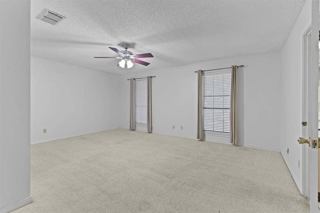 1656 Pineview Lane, Hideaway, TX 75771 Expansive room featuring light-colored carpeting, two windows with blinds, a ceiling fan with integrated lighting, and a white paneled door