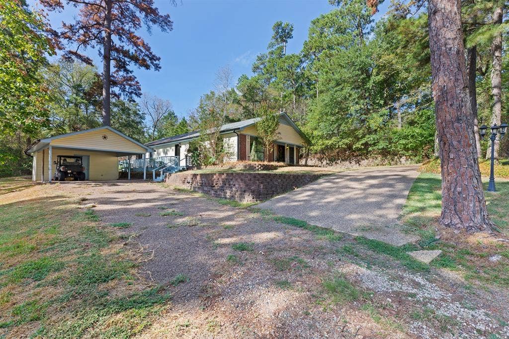 1656 Pineview Lane, Hideaway, TX 75771 Detached carport with covered parking, elevated main residence, gravel driveway, and a retaining wall