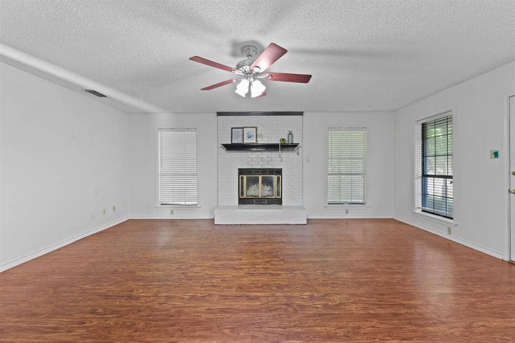 1656 Pineview Lane, Hideaway, TX 75771 Spacious room featuring wood-finish flooring, a white brick fireplace, and multiple windows with blinds