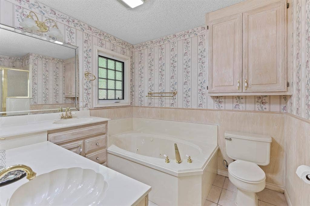 1656 Pineview Lane, Hideaway, TX 75771 Dual vanity with shell-shaped basin, corner soaking tub, integrated toilet, and built-in upper cabinetry