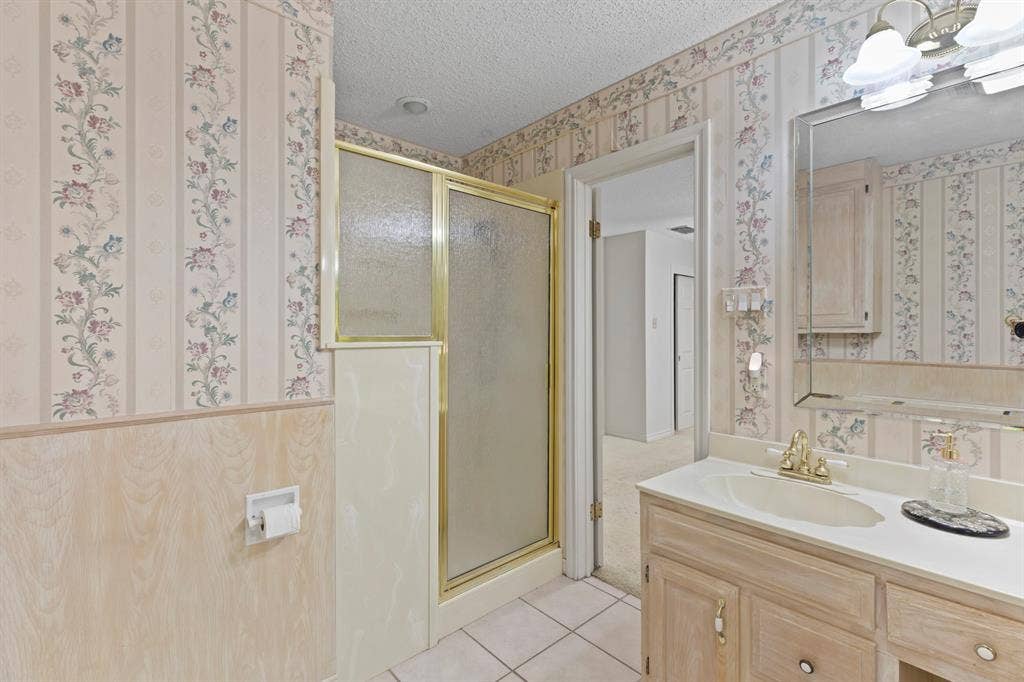 1656 Pineview Lane, Hideaway, TX 75771 Bathroom featuring a vanity with an integrated sink, a mirrored medicine cabinet, a shower enclosure with a gold-tone frame, and floral wallpaper