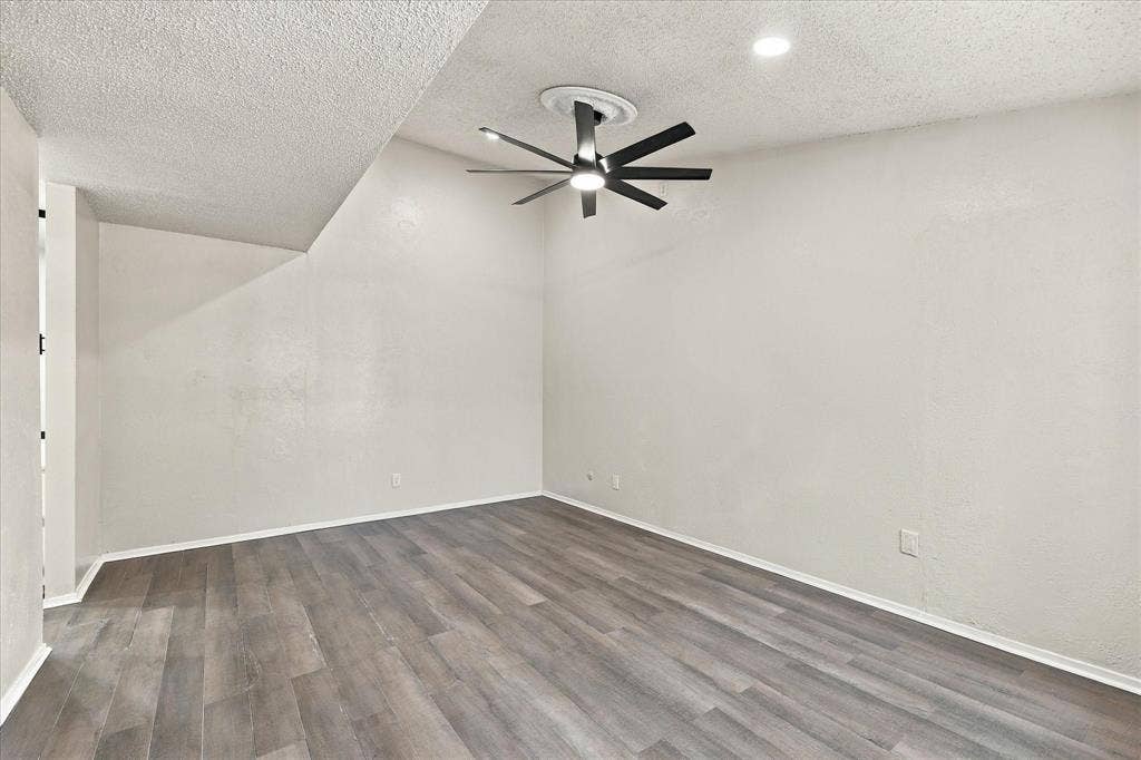 Wood-finish flooring with crisp white baseboards, featuring a modern ceiling fan and recessed lighting