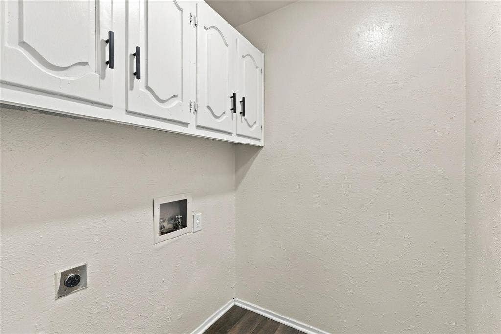 White upper cabinetry with black hardware, wood-finish flooring, and laundry hookups