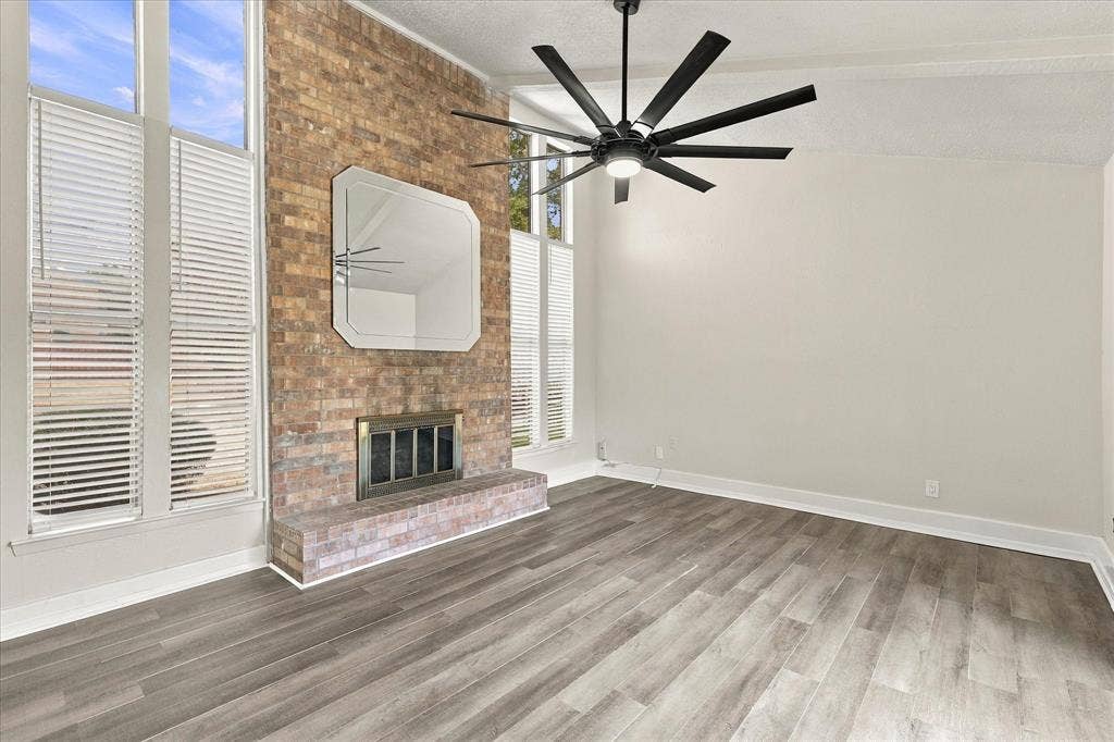 Brick fireplace with a hearth, wood-finish flooring, and a ceiling fan