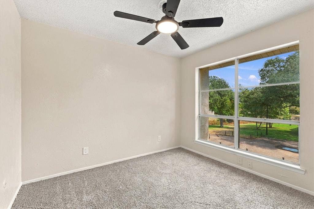 Wall-to-wall carpeting, large window with outdoor scenery, and a ceiling fan with integrated lighting
